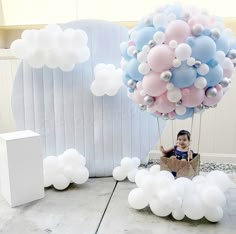 a little boy sitting in a box with balloons floating over him and the balloon is shaped like an elephant