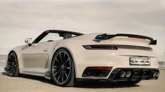 the rear end of a white sports car parked on top of a parking lot next to the ocean