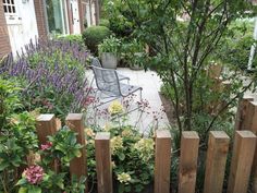 a garden with flowers, plants and a chair on the ground in front of a house