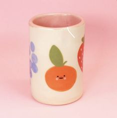 a white cup with an orange and blue design on it's side, against a pink background