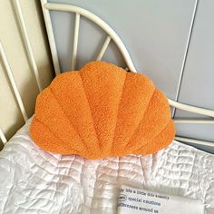 an orange pillow sitting on top of a white bed