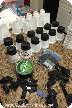 many white and black cups are on the counter next to other plastic containers, including one for each cup