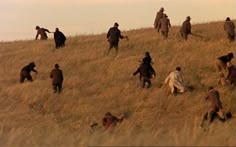 a group of people walking up a hill in the middle of an open field with tall grass