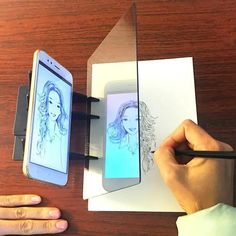 a person is drawing with a pencil on paper and an electronic device next to it