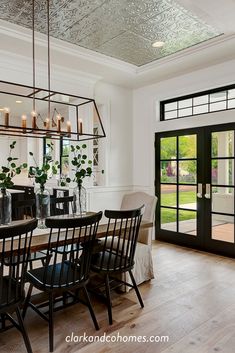 a dining room table and chairs with candles on the chandelier above them in front of a glass door