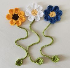 three crocheted flowers on a white surface with green stems and two yellow ones