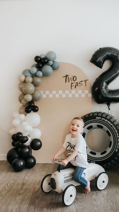 a young boy is sitting on a toy car in front of balloons and an age sign