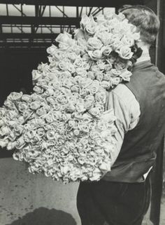 a man carrying a large bouquet of flowers on his back to the camera in black and white