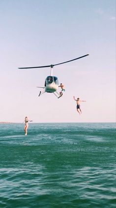 three people jumping into the water from a helicopter in the air, while another person dives