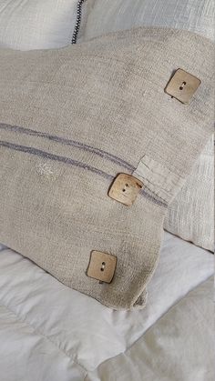 two pillows with buttons on them are sitting on a white comforter, one is made out of linen and the other has an old buttoned down pillow