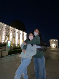 two people hugging each other in front of a building at night with the lights on