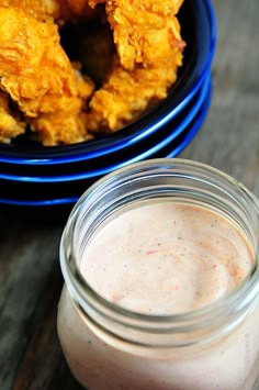 a glass jar filled with sauce next to some fried food