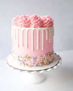 a pink frosted cake with sprinkles and icing on a plate