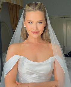 a woman wearing a white wedding dress with a veil on her head, posing for the camera