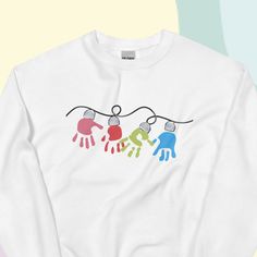 Christmas Lights Sweater | Holiday Handprint Sweatshirt | Holiday Lights DIY Art | Children's Holiday Craft | Gifts for Grandparents DIY gift for family! Use fabric paint to create a one-of-a-kind gift they'll keep forever. A sturdy and warm sweatshirt bound to keep you warm in the colder months. A pre-shrunk, classic fit sweater that's made with air-jet spun yarn for a soft feel and reduced pilling. * 50% cotton, 50% polyester * Pre-shrunk * Classic fit * 1x1 athletic rib knit collar with spand Puff Paint Christmas Sweatshirt Diy, Handprint Sweatshirt, Holiday Craft Gifts, Puffy Paint Christmas Shirt, Puffy Paint Christmas Sweater, Craft Gifts For Grandparents, Kids Christmas Shirts Vinyl Custom, Kids Ornament Sweater, Kids Christmas Crewneck