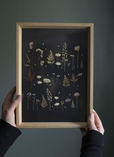 a person holding up a framed art piece with flowers on black paper in front of them