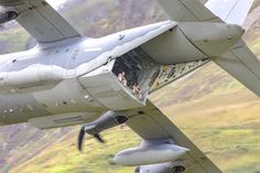 an airplane with people in it is flying over the grass and hills behind it are mountains