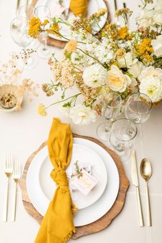 the table is set with yellow napkins and white plates, silverware, and flowers