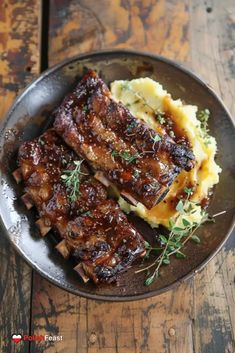 some meat and mashed potatoes are on a black plate with green garnish