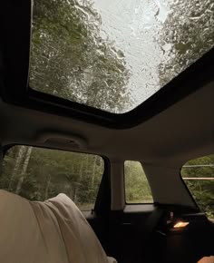 the inside of a car with rain on the windshield and trees in the back ground