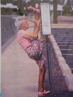 an older woman leaning up against a pole on the side of a road with her feet in the air