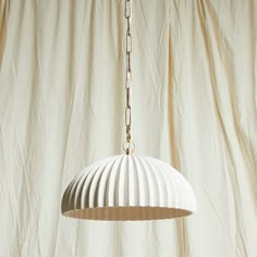 a white lamp hanging from a gold chain on a beige curtained room with curtains in the background