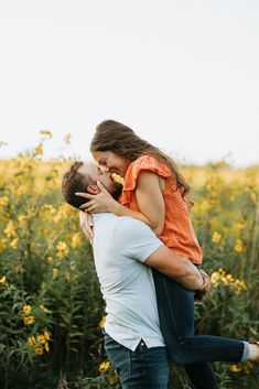 a man holding a woman in his arms while she is walking through a field full of yellow flowers