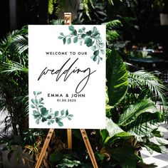 an easel with a sign that says welcome to our wedding on it in front of some plants