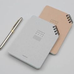 two notebooks and a pen sitting next to each other