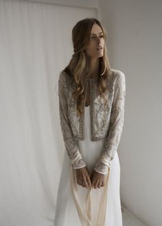 a woman standing in front of a white backdrop wearing a dress and jacket with long sleeves