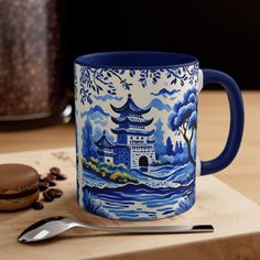 a blue and white coffee mug sitting on top of a wooden table next to a cookie