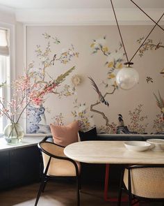 a dining room table and chairs with birds painted on the wall behind it in front of a window