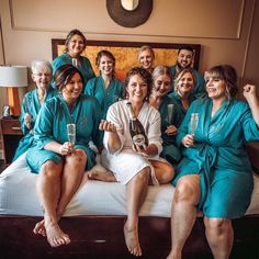 a group of women sitting on top of a bed in blue robes holding champagne flutes