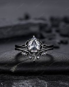 a white diamond ring sitting on top of a black stone slab with stones in the background