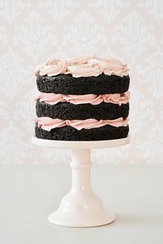 a chocolate cake with pink frosting on a white pedestal