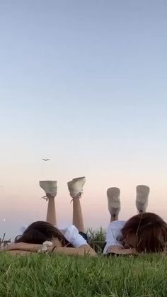 two people laying on the grass with their feet up in the air and birds flying overhead