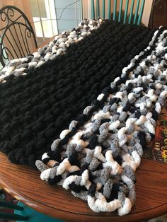 there is a black and white crocheted blanket on top of a table next to a chair