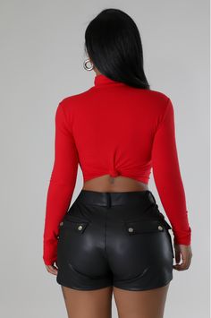 a woman in black leather shorts and a red top is looking back at the camera