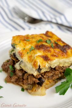 a white plate topped with lasagna covered in meat and cheese on top of green garnish