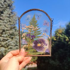 a hand holding up a glass frame with flowers and butterflies on it