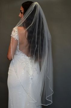 a woman in a wedding dress wearing a veil and looking at the back of her gown