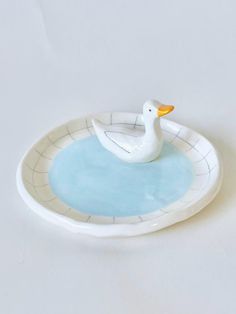 a white duck sitting on top of a bowl filled with blue water in front of a white background