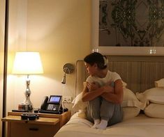 a woman sitting on top of a bed next to a phone and lamp in a room