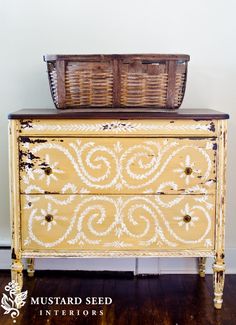 an old dresser has been painted yellow with white swirls and is next to a basket on top