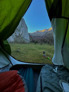 the view from inside a tent looking out at a mountain range and grassy field with tents