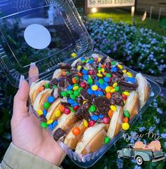 a person holding up a plastic container filled with lots of candy covered doughnuts