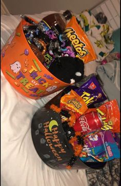 two buckets filled with halloween candy on top of a white bed covered in sheets