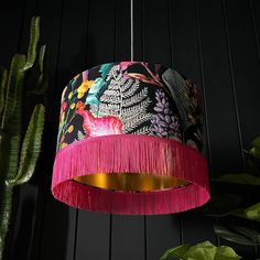 a pink lamp hanging from a ceiling next to a cactus