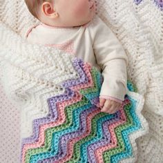 a baby laying on top of a blanket next to a white and blue blanket with a crochet pattern