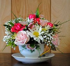 a teacup filled with flowers on top of a wooden table